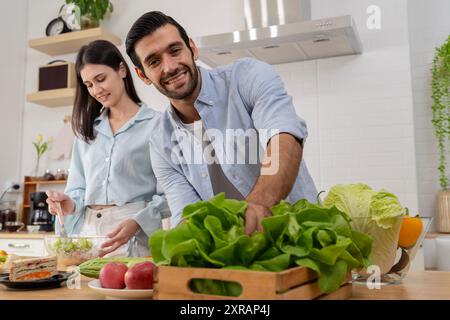 Eccitato sorridente giovane coppia innamorata facendo un'insalata vegana super sana con molte verdure in cucina e l'uomo che la prova dalle mani di una ragazza Foto Stock