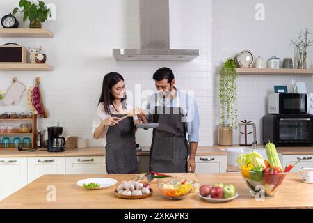 Una coppia romantica sta cucinando in cucina. Un bell'uomo e una giovane donna affascinante si divertono insieme mentre preparano l'insalata. Stile di vita sano con Foto Stock