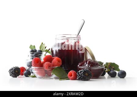 Marmellata di frutti di bosco con vasetti pieni e contenitori con lamponi, more e mirtilli su sfondo bianco isolato riflesso alla base. Fron Foto Stock