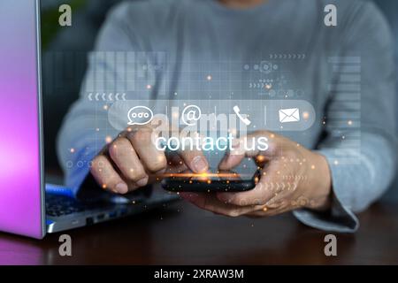 Contattaci o contatta il servizio di assistenza clienti. Uomo d'affari che utilizza smartphone, laptop e tocca le icone dei contatti sullo schermo virtuale. Sito Web e. Foto Stock