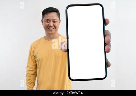 Uomo sorridente e soddisfatto che mostra il mockup bianco del telefono cellulare con la fotocamera in piedi isolata nello spazio di copia dello studio. Primo piano dello smartphone Foto Stock