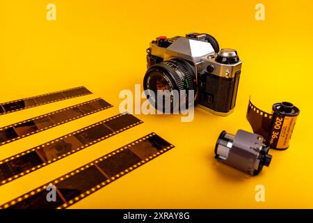 Primo piano di una fotocamera d'epoca abbinata a rotoli di pellicola usati da 35 mm su sfondo giallo, che mettono in risalto la bellezza della fotografia analogica. Foto Stock