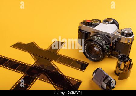 Una macchina fotografica d'epoca e rotoli di pellicola sviluppati da 35 mm occupano il centro della scena su uno sfondo giallo, evocando ricordi dell'epoca d'oro della fotografia cinematografica. Foto Stock