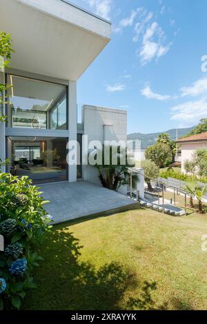 Giardino verde e ingresso di una casa moderna bianca. Soleggiata giornata estiva e cielo azzurro. Nessuno dentro Foto Stock