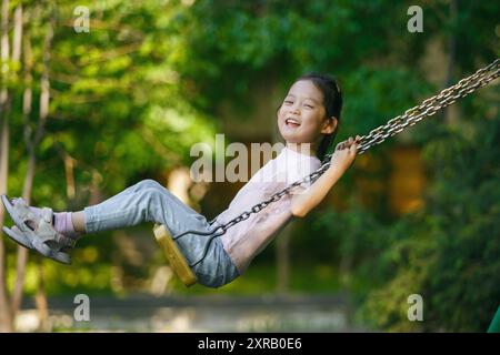 La ragazza cinese sorridente oscilla sul parco giochi Foto Stock