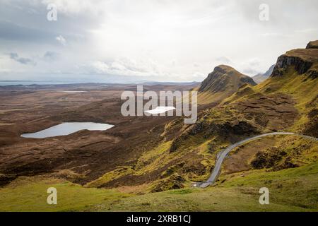 Vista panoramica della frana di Quiraing sull'isola di Skye, in Scozia, con aspre colline e laghi sotto un cielo nuvoloso Foto Stock