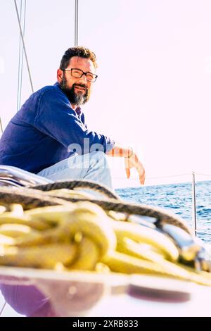 Ritratto dell'uomo siediti sul ponte della barca a vela e guarda lontano all'oceano - gli adulti maschi godono di viaggi e stile di vita - immagine concettuale marina e di navigazione - cielo luminoso sullo sfondo - escursione estiva Foto Stock