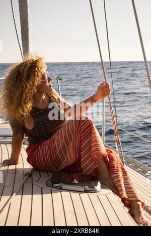 Il concetto di stile di vita del viaggio in barca a vela con una bella giovane donna adulta siediti sul ponte e goditi l'avventura di viaggio - le donne godono della natura dell'oceano all'aperto sulla barca Foto Stock