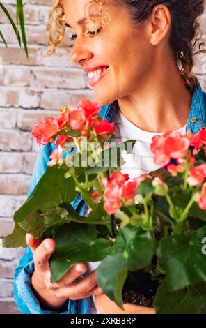 Ritratto di donna felice che tiene fiori e pianta a casa contro un muro di mattoni sfondo. Le donne sorridono dopo aver ricevuto un regalo naturale. Anniversario e compleanno concetto presente Foto Stock