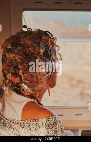 Vista sul retro della donna che si affaccia fuori dalla finestra del camper. Vita in furgone e stile di vita dei viaggiatori. Libertà di vivere fuori dalla griglia in un veicolo e casa alternativa su ruote. Concetto di vita Foto Stock