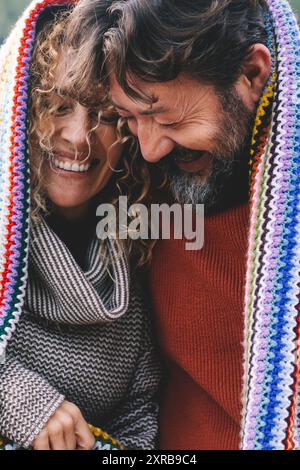 Overjoyed coppia caucasica adulta sotto una copertura colorata ridere e divertirsi insieme con amore e amicizia. Giovani maturi in attività romantiche all'aperto per il tempo libero. L'uomo e la donna ridono molto Foto Stock