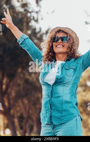 Gente overjoyed donna felice alzando le braccia con il gesto di vittoria e sorridendo con gli alberi verdi natura all'aperto sfondo. Allegre donne in attività turistiche fuori. Signora che si diverte Foto Stock