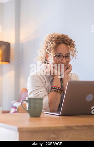 Alla testa una giovane donna freelance felice che lavora al computer a casa. Attraente donna d'affari che studia online, utilizza software per computer portatili, informazioni di navigazione sul Web o fa shopping in un negozio Internet. Foto Stock