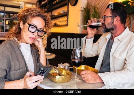 Una coppia infelice che si ignora in un ristorante che guarda il cellulare - una coppia sposata arrabbiata che pranza al bar - concetto di persone Foto Stock