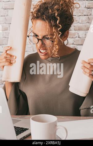 Donna arrabbiata di fronte a un computer con espressione cattiva e stressata. Donna stanca che lavora su un computer portatile in un ufficio domestico. Concetto di problemi con il lavoro e la tecnologia. Persone in una vita lavorativa intelligente Foto Stock
