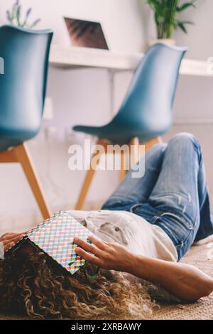 Una donna a casa si stese sul tappeto coprendo il suo viso con un libro. Concetto di istruzione e di mezza età per studenti. Donne che dormono per terra nell'appartamento. Stile di vita stanco e stressato Foto Stock