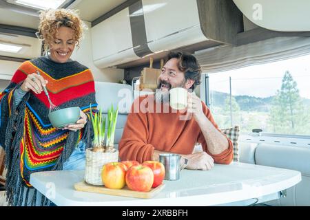 Coppie giovani e mature si godono la vita in un camper camper insieme in attività ricreative al coperto. Vista sulla natura fuori dalla finestra. Viaggiatore felice persone uomo e donna all'interno di un furgone per le vacanze Foto Stock