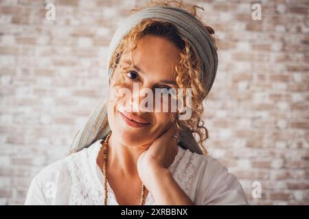 Una donna felice e riccia sorride guardando la telecamera. Ritratto frontale di una signora di mezza età con sfondo in mattoni. Una bella donna di mezza età che sorride e ti guarda. Allegra signora Foto Stock