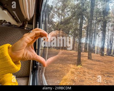 La donna mette la mano sul vetro formando un cuore con il riflesso. Concetto di gioco e amore per la natura Foto Stock