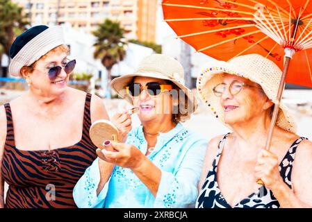 Tre donne mature che indossano cappelli da spiaggia e sorridono mentre sono in piedi su una spiaggia tropicale. Le donne più anziane si divertono nelle attività ricreative all'aperto nello stile di vita estivo delle vacanze. Vita di amici anziani Foto Stock