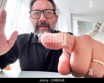 Un uomo adulto impegnato in una videoconferenza puntando il dito sullo schermo nella vista della telecamera. Persone e comunicazioni online con webcam su laptop o dispositivo telefonico. Un moderno uomo d'affari che viaggia da remoto Foto Stock