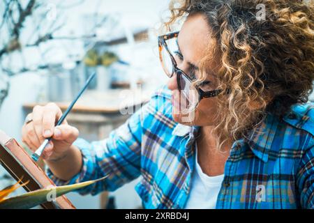 Giovane bella donna adulta pittrice crea quadri, disegnando con pitture su tela in un moderno laboratorio. Professione professionale, hobby creativo, attività per l'anima, vocazione, sviluppare il concetto di abilità Foto Stock