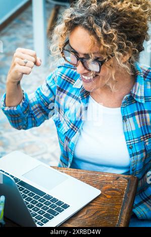 Eccitata donna caucasica matura sedersi alla scrivania sentirsi euforica vincere lotteria online, felice signora adulta felicissima ottenere posta al portatile che viene promosso al lavoro, persone occasionali stupito leggere buone notizie al computer Foto Stock