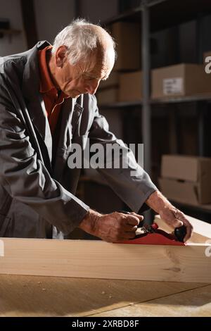 Falegname che utilizza una pialla manuale per la lavorazione del legno nella sua officina. Abile artigiano che lavora con il legno per creare precisi oggetti in legno, dimostrando Foto Stock