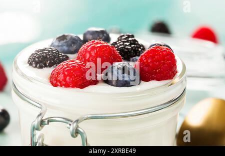 Un vasetto di yogurt con mirtilli, more e lamponi sul vassoio in legno Foto Stock