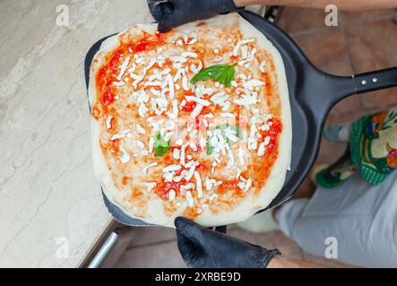 Materie pizza margherita messo sulla pala da forno per la cottura. Foto Stock