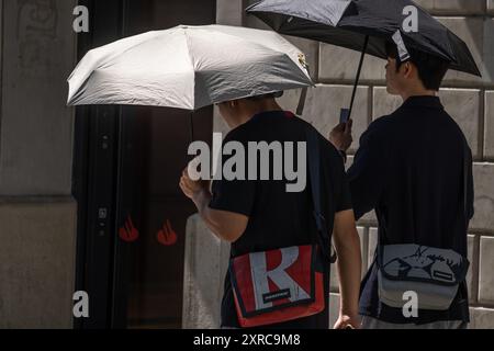 Barcellona, Spagna. 09 agosto 2024. Due turisti asiatici hanno visto proteggersi dal sole con gli ombrelloni mentre passeggiavano lungo il centro commerciale Passeig de Gràcia. Barcellona soffre ancora una volta di un'ondata di caldo con temperature che raggiungono i 40 gradi Celsius sull'asfalto del centro città. Credito: SOPA Images Limited/Alamy Live News Foto Stock