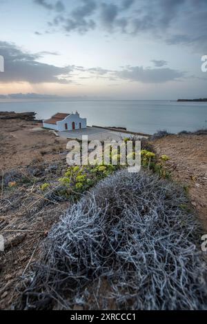 Piccola chiesa bianca in tipico stile architettonico greco, situata su una roccia lavica, circondata dal Mar Mediterraneo, Cappella di Agios Nikolaos all'alba, Zante, Isole Ionie, Grecia Foto Stock