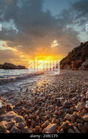 Baia nascosta sul Mar Mediterraneo all'alba, piccola spiaggia di sabbia e ciottoli nei colori caldi dell'alba, vista del mare a Xigia Sulfur Beach, Zante, Isole Ionie, Grecia Foto Stock