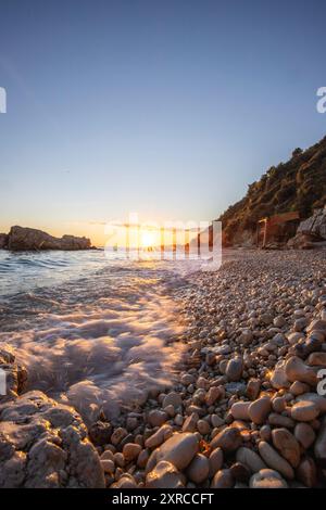 Baia nascosta sul Mar Mediterraneo all'alba, piccola spiaggia di sabbia e ciottoli nei colori caldi dell'alba, vista del mare a Xigia Sulfur Beach, Zante, Isole Ionie, Grecia Foto Stock