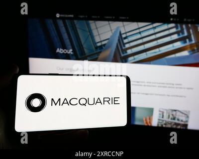 Persona con smartphone con logo della società finanziaria australiana Macquarie Group Limited davanti al sito Web. Mettere a fuoco il display del telefono. Foto Stock