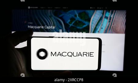 Persona che detiene un cellulare con il logo della società finanziaria australiana Macquarie Group Limited di fronte alla pagina web aziendale. Mettere a fuoco il display del telefono. Foto Stock