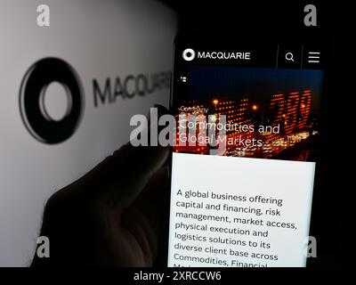 Persona che detiene un cellulare con pagina web della società finanziaria australiana Macquarie Group Limited davanti al logo. Messa a fuoco al centro del display del telefono. Foto Stock