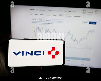 Persona che possiede un telefono cellulare con il logo della società francese Vinci SA di fronte alla pagina web aziendale. Mettere a fuoco il display del telefono. Foto Stock