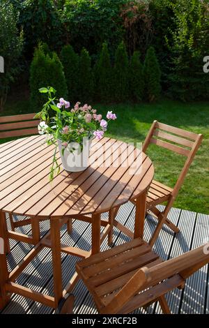 Su un tavolo di legno nel giardino si erge un vaso di fiori bianco con fiori freschi bianchi e rosa, fiori fioriti alla luce del sole in tarda estate Foto Stock