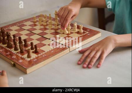 Primo piano focalizzato delle mani dei bambini che muovono pezzi di scacchi durante una partita su una scacchiera di legno. Attività didattica e strategica per i bambini. Foto Stock