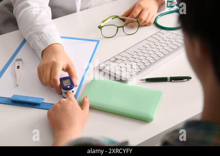 Medico femminile che prende polso da paziente a scrivania medica bianca, primo piano Foto Stock