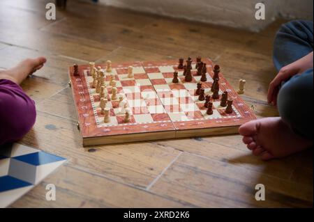 Un primo piano di due persone che giocano a scacchi su un pavimento di legno. Le gambe dei giocatori sono visibili, creando un'atmosfera informale e intima intorno al classico Foto Stock