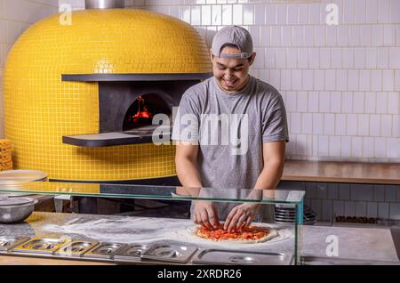 Cuocere a mano per preparare una pizza, mettere la salsiccia sopra. Spolverare a mano il formaggio sull'impasto della pizza con salsa di pomodoro. Processo di preparazione della pizza. Chef meticolosamente Foto Stock