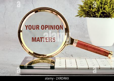Un cartello di testo che mostra LA TUA OPINIONE È IMPORTANTE sulla lente d'ingrandimento di fronte a una parete grigia, sfondo Foto Stock