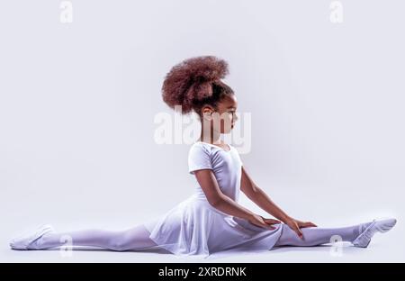 Ballerina in un filetto bianco. Una piccola ballerina che giace per terra. Piccola ballerina afroamericana flessibile. Ballerina in classe di danza Foto Stock