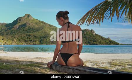 La donna gode pacificamente del sole caldo e della vista mozzafiato su una spiaggia appartata nei maupiti. polinesia francese. Creando un paradiso idilliaco perfetto per rilassarsi e immergersi nella bellezza della natura Foto Stock