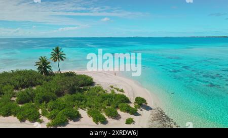 Vista aerea di una donna che cammina su una spiaggia incontaminata di sabbia bianca, circondata da acque turchesi e da una lussureggiante vegetazione verde. La destinazione perfetta per una vacanza rilassante e indimenticabile Foto Stock