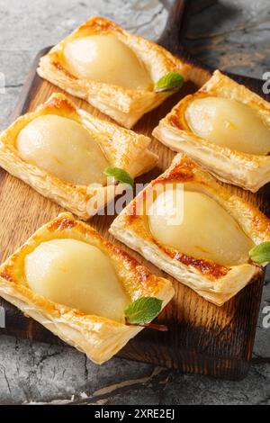 Pere autunnali cotte in pasta sfoglia e ripiene di noci e formaggio spalmabile sul bordo di legno sul tavolo. Verticale Foto Stock