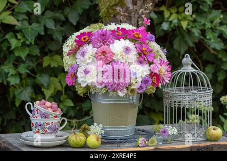 disposizione dei tavoli con bouquet di dalie, zinnie, garofani e carote selvatiche, coppe di porcellana e gabbia per uccelli nel giardino Foto Stock