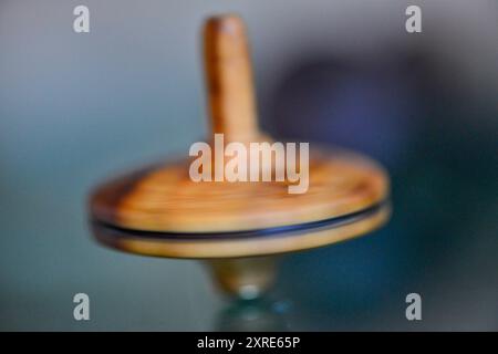 Una foto macro di un teetotum in legno che gira e si trova su una superficie di vetro, che mostra la sua intricata maestria artigianale e la superficie liscia e riflettente. Foto Stock